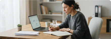 A person taking notes while working on a laptop